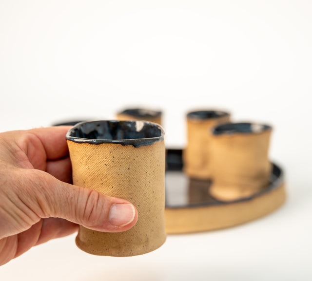 Round stoneware tray and six cups, alternate view showing blue-black glaze breaking at the rims, J Schatz