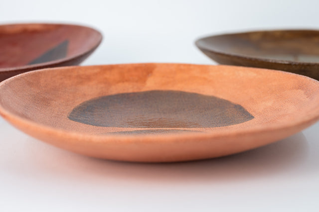 Geometria bowls in glazed stoneware seen from the side, a terracotta bowl with dark half-circles in front, by Jim Schatz, J Schatz