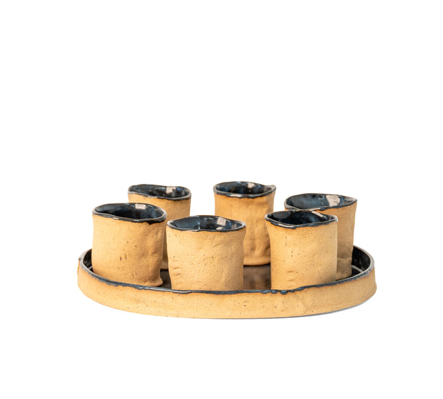 Round stoneware tray with six hand-built cups, raw speckled clay with blue-black glazed interiors, J Schatz